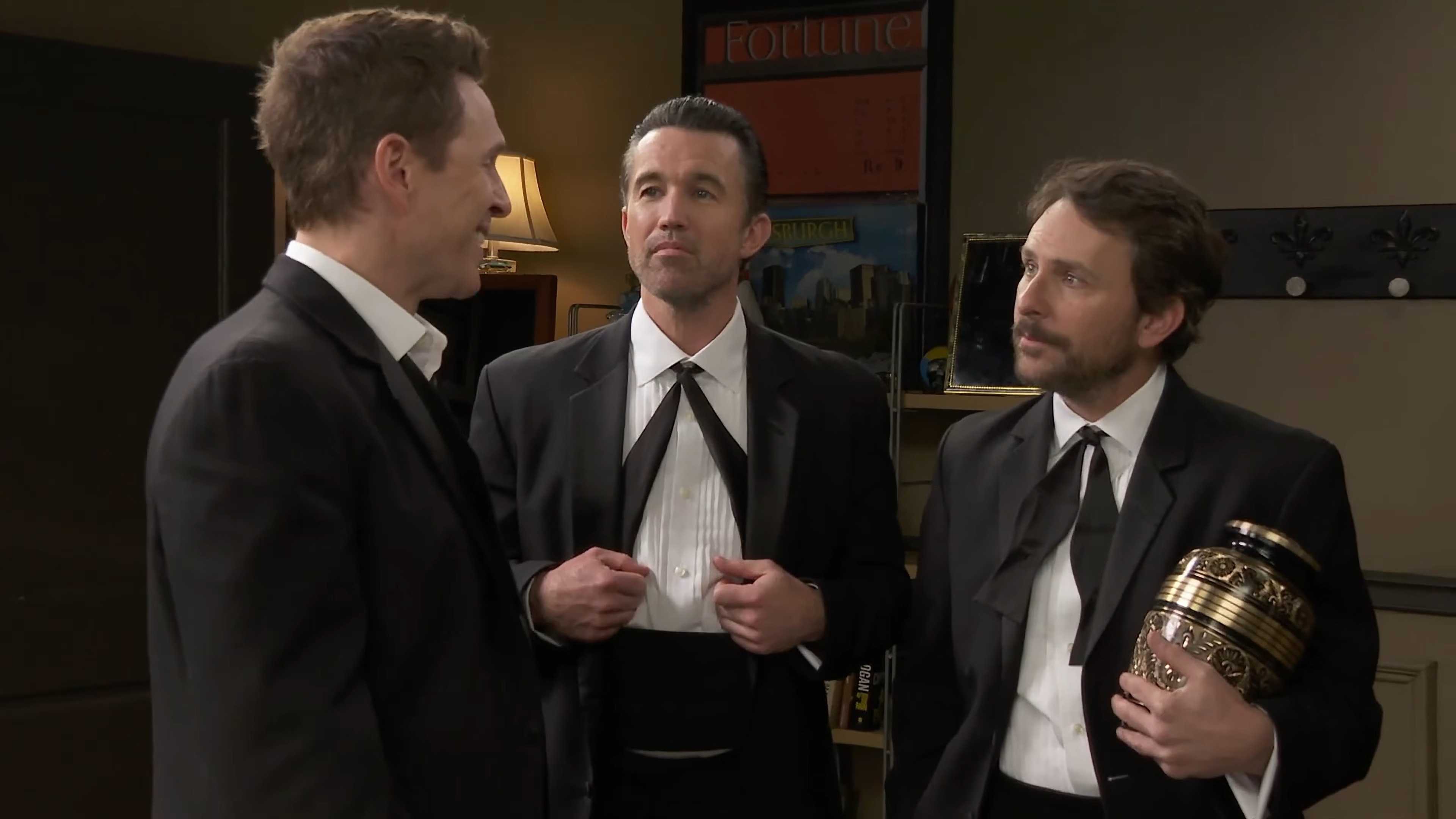 Mac de Rob Mac sonriendo levemente y Charlie de Charlie Day sosteniendo una urna mientras mira a Dennis de Glenn Howerton en It's Always Sunny in Philadelphia temporada 18