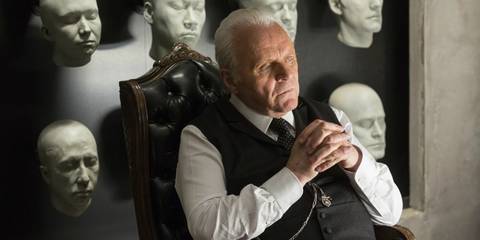 Robert Ford (Anthony Hopkins) sitting and looking thoughtful in front of a wall of host faces