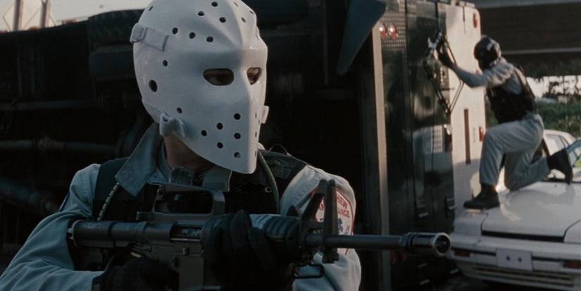 A robber in a hockey mask holds up his rifle while another robber attempts to break into a truck in the background in Heat