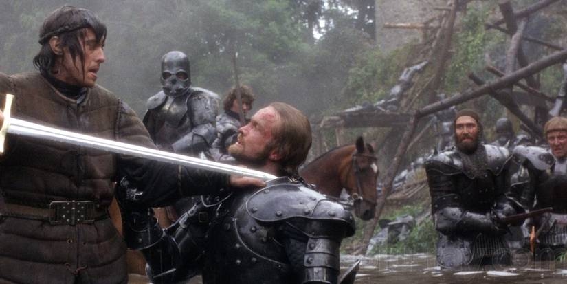 Uma imagem de uma pessoa segurando uma espada na garganta de seu inimigo no filme Excalibur