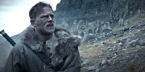 Charlie Hunnam as King Arthur walks over rought terrain in King Arthur: Legend of the Sword