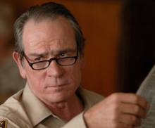 Шериф Эд Том Белл, смотрящий в свой газету в фильме *No Country for Old Men*