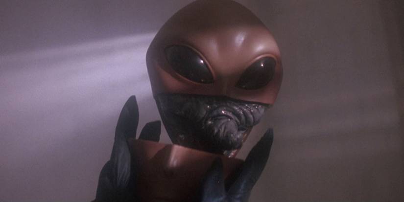 A grey alien removes its mask in Communion