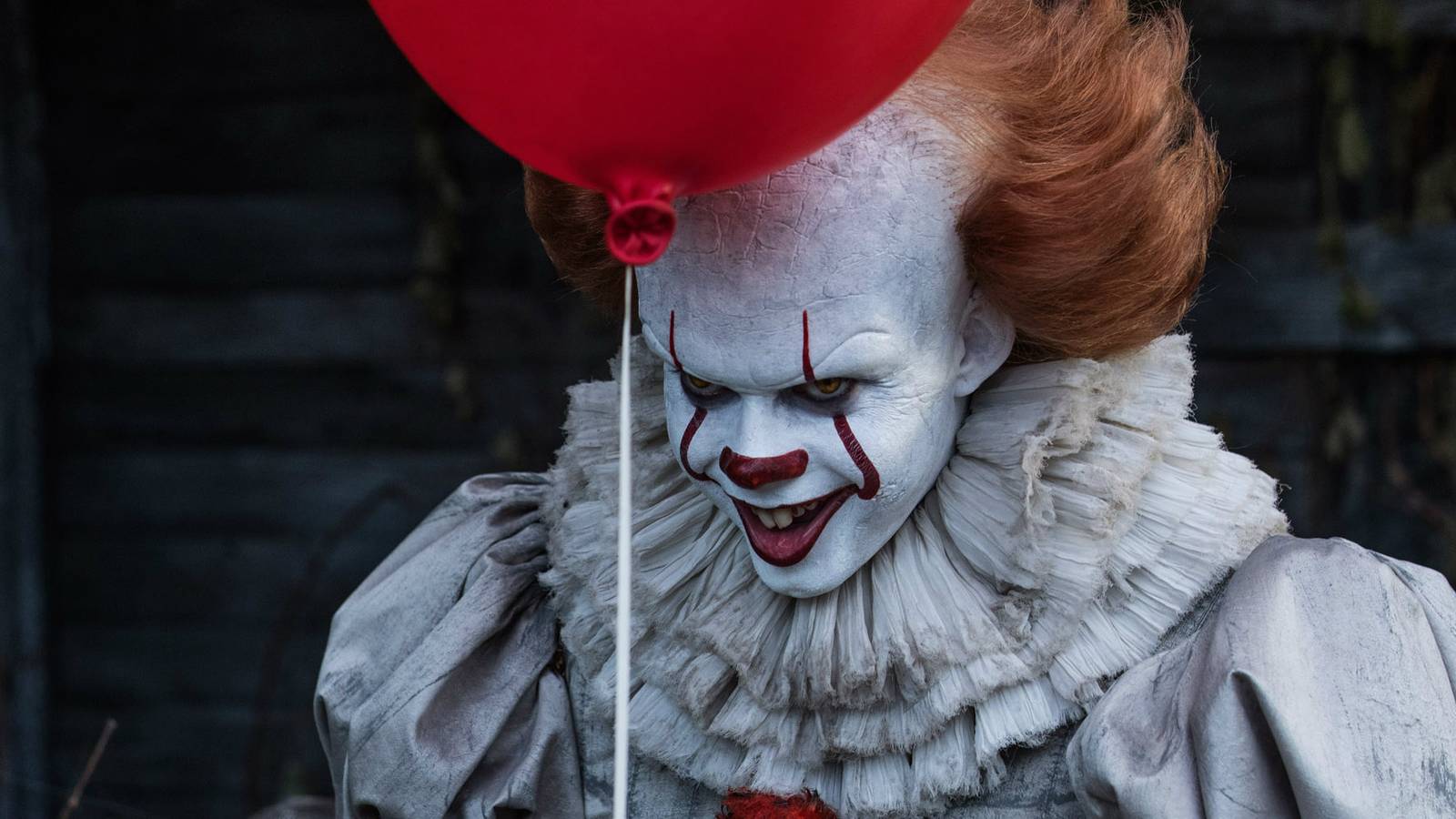 Pennywise smiling and holding a red balloon in IT