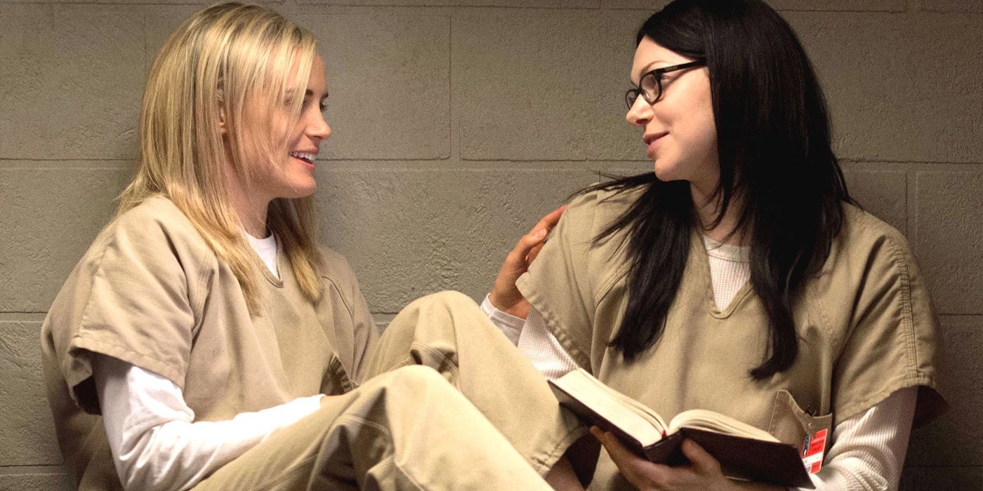 Piper (Taylor Schilling) and Alex (Laura Prepon) sitting together in their cell with a book in Orange is the New Black