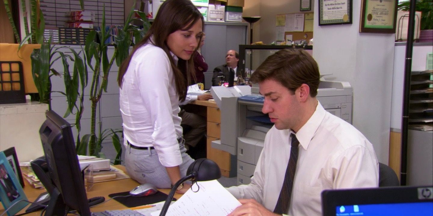 Karen sitting on Jim's desk while Jim works in The Office.