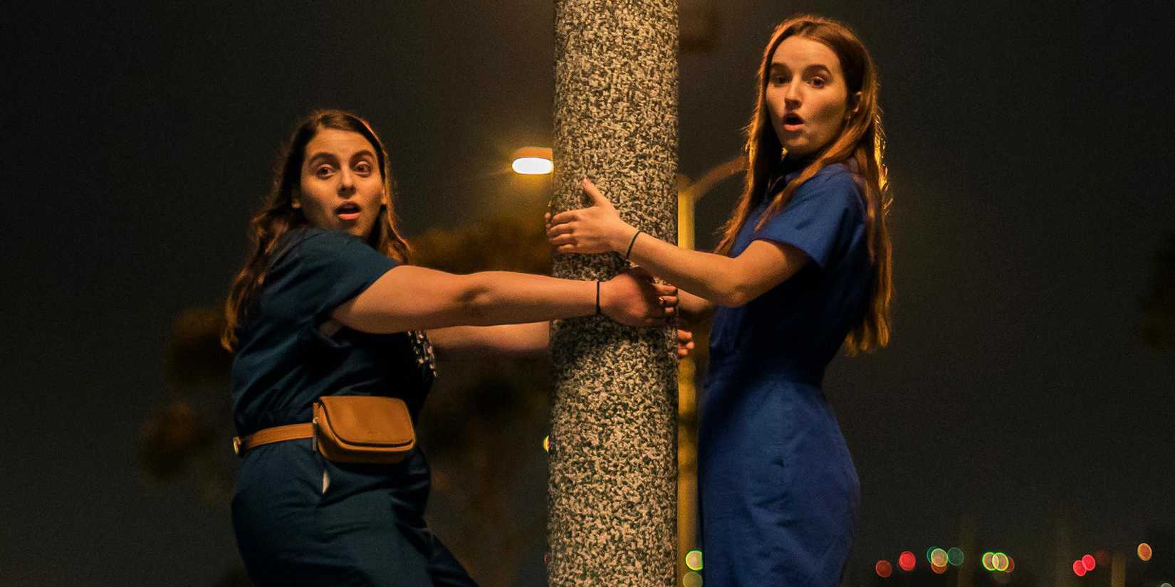 Beanie Feldstein e Kaitlyn Dever segurando um poste em Fora de Série