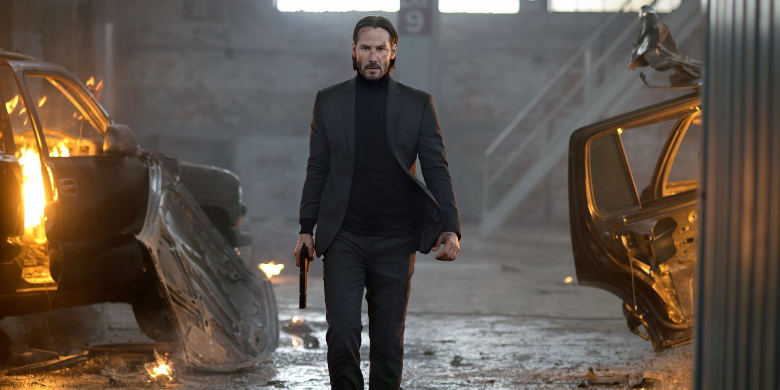 Keanu Reeves holding a pistol in a warehouse with destroyed cars in John Wick 2014