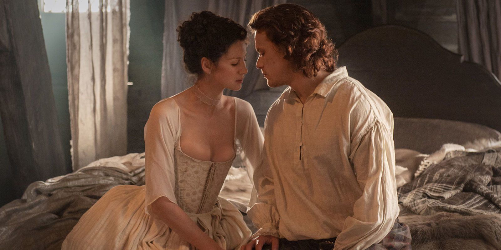 Jamie and Claire Fraser sit on their bed and lean in to kiss in Outlander