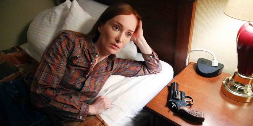 Katarina Rostova lying by a bed with a gun in The Blacklist
