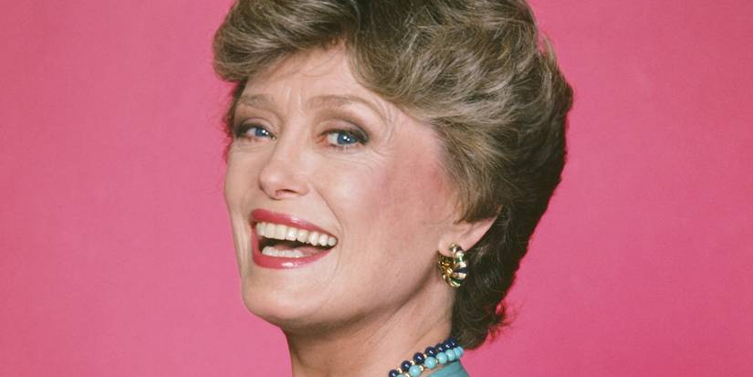Rue McClanahan smiling in front of a pink background as Blanche in The Golden Girls