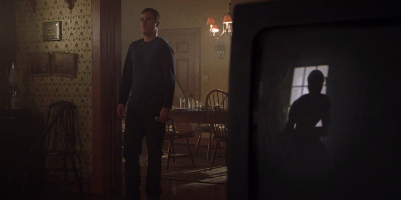 Joaquin Phoenix's Merrill stands beside the reflection of an alien on a TV screen in Signs