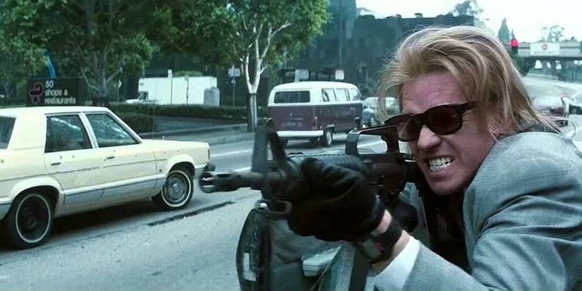 Val Kilmer pointing a gun and firing down the street with a grimace in Heat