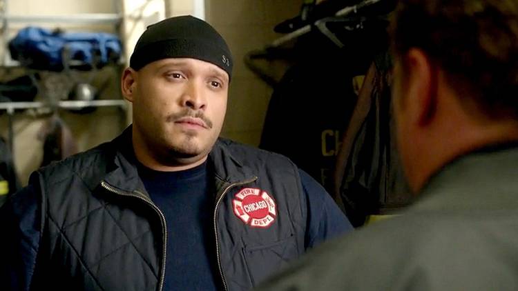 Joe Cruz wearing a Chicago One vest in front of fire jackets in Chicago Fire