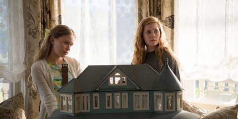 Camille Preaker (Amy Adams) and Amma Crellin (Eliza Scanlen) sitting behind a dollhouse in Sharp Objects.
