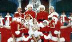 The cast of the musical within White Christmas posing as they sing in red and white outfits
