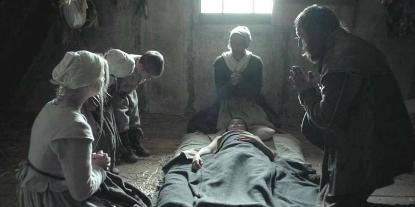 Family members praying around each other in The Witch. 