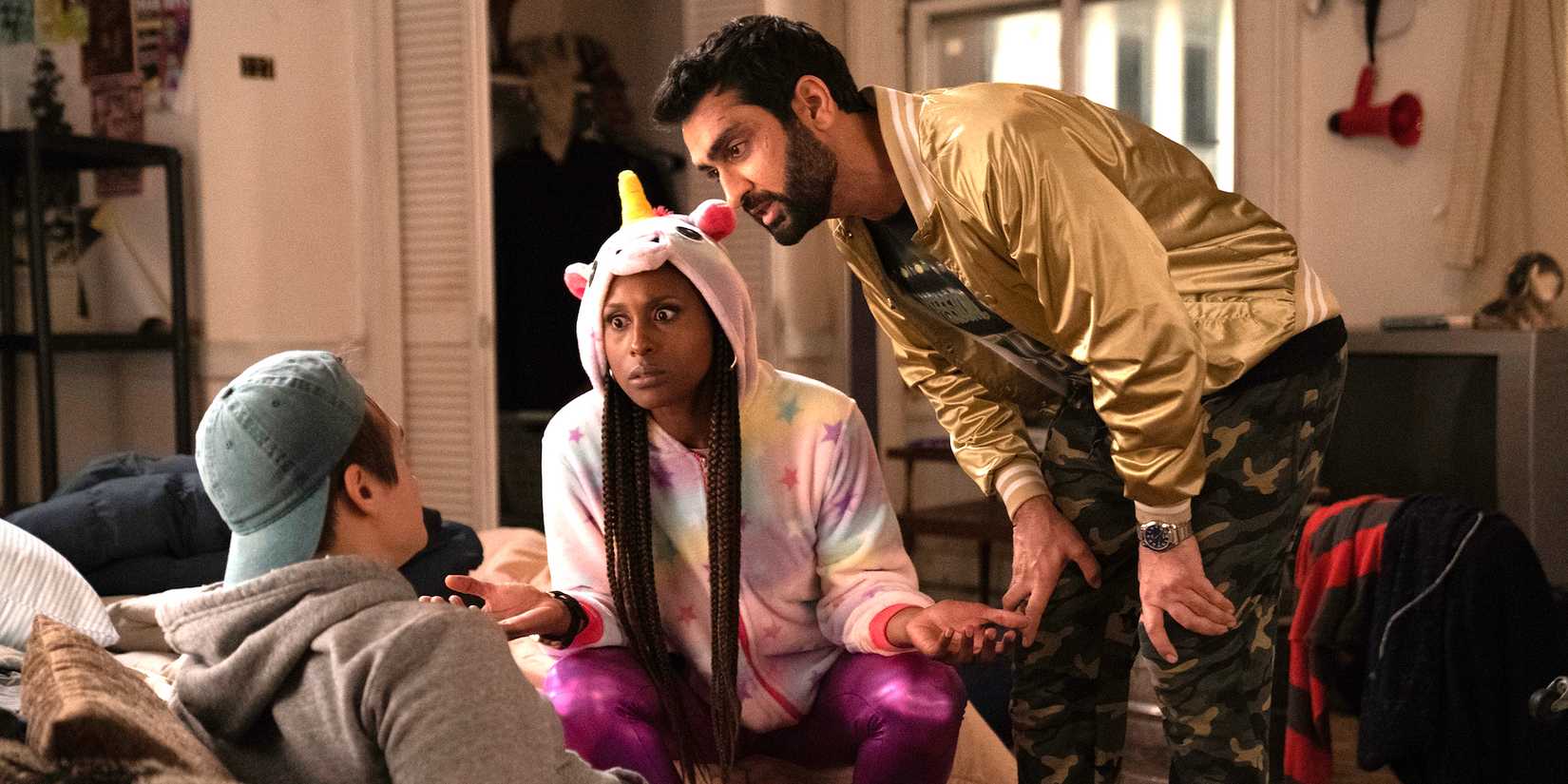 Kumail Nanjiani wears a gold metallic jacket and Issa Rae wears a unicorn hoodie in The Lovebirds