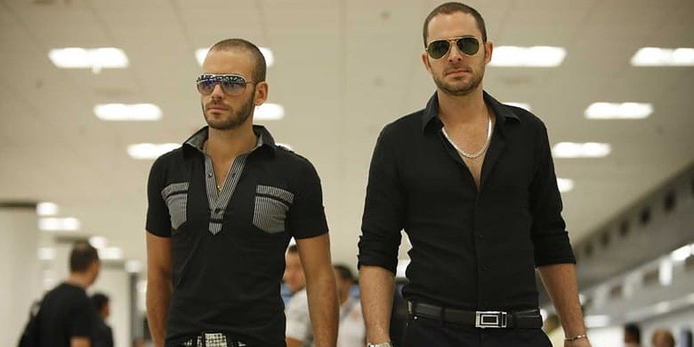 Two men walking in an airport with sunglasses on in The Snitch Cartel