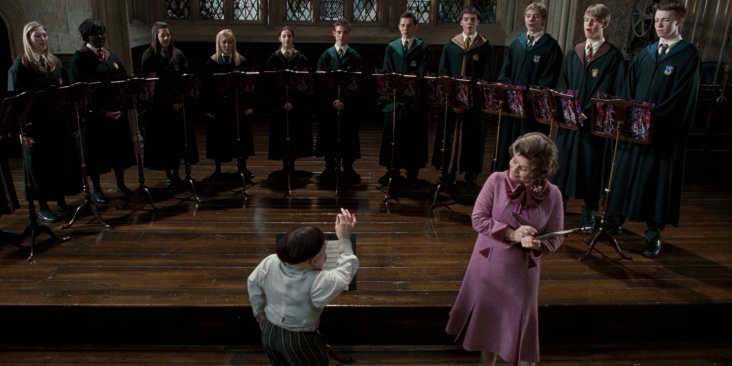 Professor Flitwick conduzindo o coral de Hogwarts enquanto a Professora Umbridge faz anotações