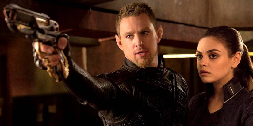 Caine pointing a gun while Jupiter stands beside him in Jupiter Ascending