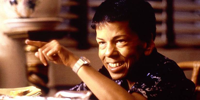 Linda Hunt as Billy Kwan smiling and pointing at something in The Year of Living Dangerously
