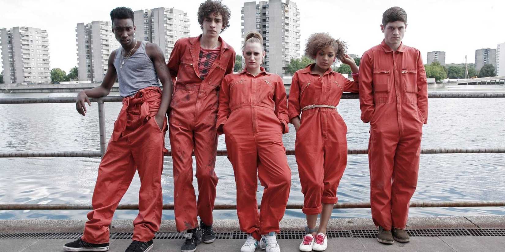 Misfits cast leaning on a railing by the river in orange jumpsuits