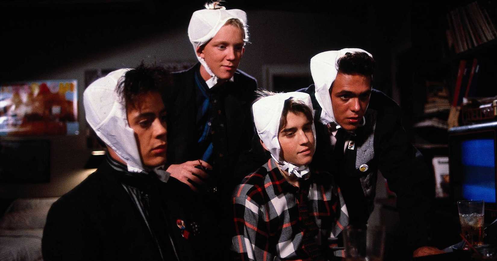 The teen boys in Weird-Science sit with braws on their heads and look at a computer. 