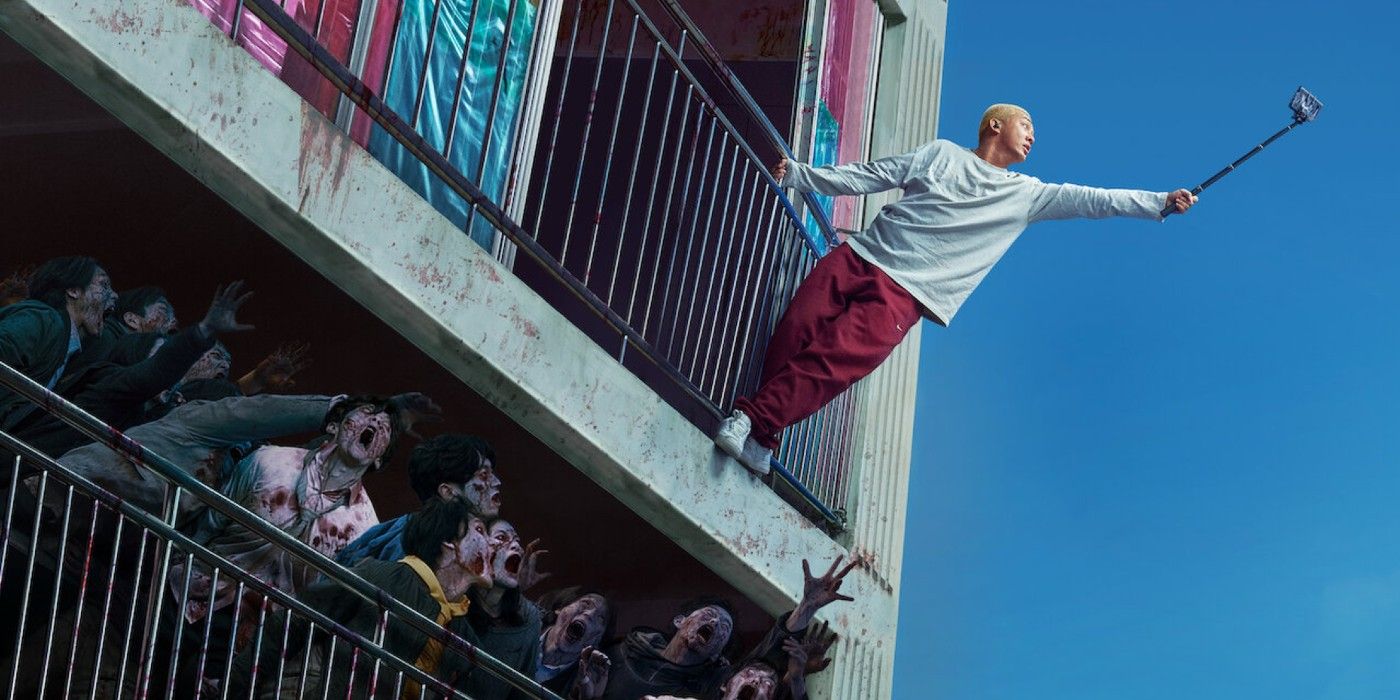 A man taking a selfie hanging off a balcony above zombies