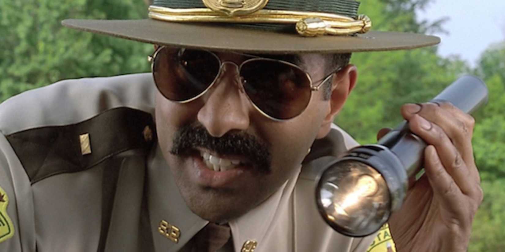 Arcot Ramathorn shining his flashlight while leaning into a car in Super Troopers.