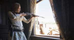 A character from Godless pointing a gun out of the window