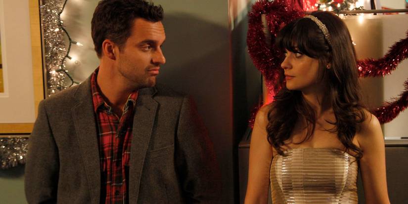 New Girl, The 23rd episode still. At a Christmas party surrounded by twinkly lights and red garland, Nick (Jake Johnson) smiles softly at Jess (Zooey Deschanel) who stares back at him.
