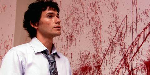 Brian Moser aka Ice Truck Killer standing beside a blood splattered wall in Dexter