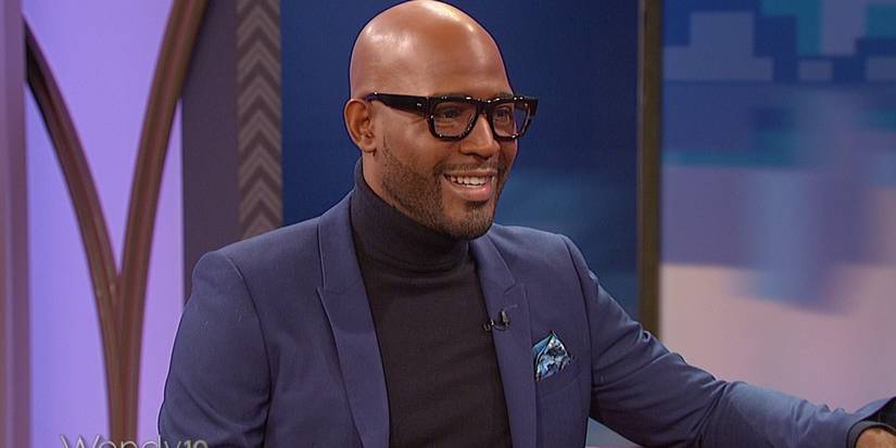 Karamo Brown wearing glasses and a suit jacket standing and smiling