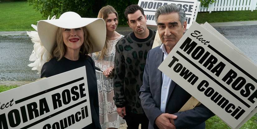 Moira, Alexis, David, and Johnny hold signs that say Elect Moira Rose Town Council in Schitt's Creek