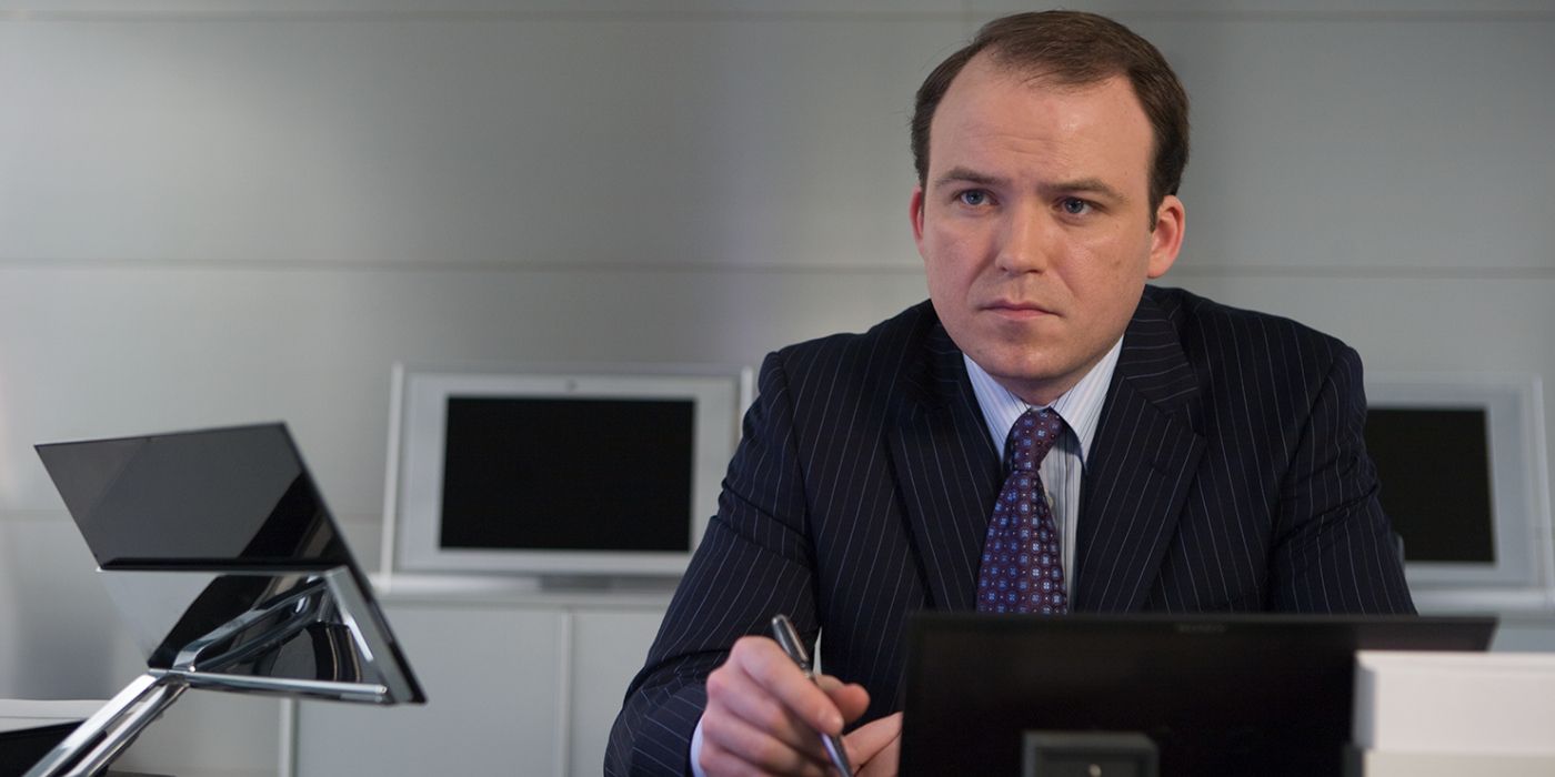 Rory Kinnear as Bill Tanner talks behind a desk in a James Bond film.