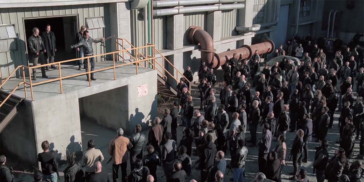 Negan standing on a balcony with the Saviors crowded around listening.