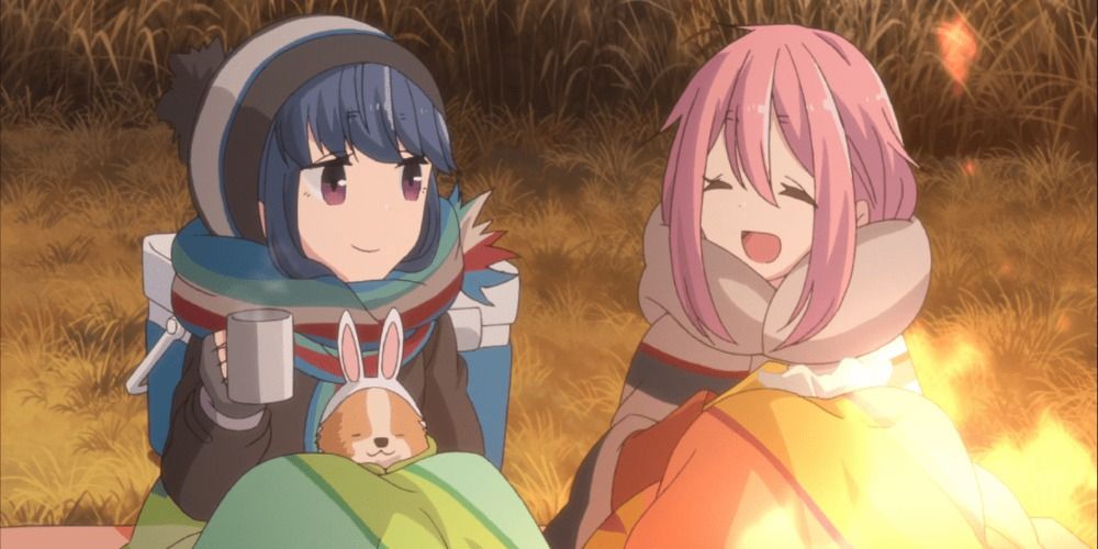 Rin and Nadeshiko of Laid Back Camp sitting by a campfire bundled up in blankets and smiling