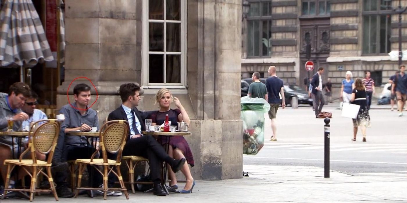 Leslie and Ben sitting outside with Mike Schur sitting behind him on Parks and Rec