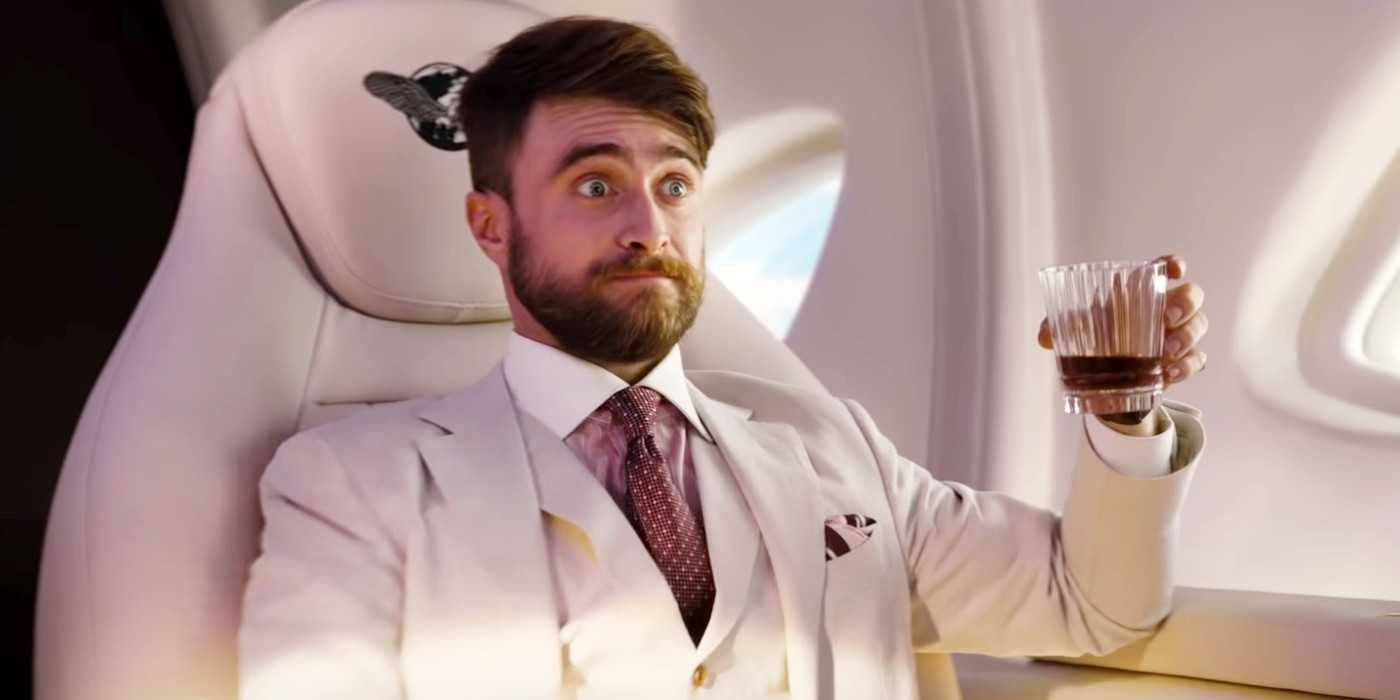 Daniel Radcliffe as Abigail Fairfax, holding a drink on a plane and looking surprised in The Lost City
