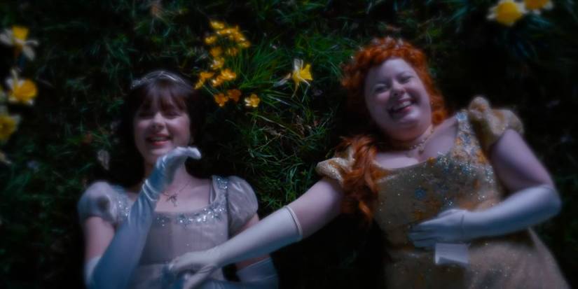 Penelope and Eloise laughing on the grass on Bridgerton