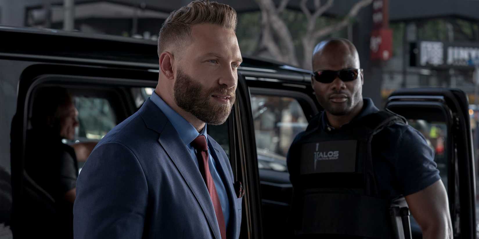 Jai Courtney wearing a suit and standing in front of a black car in The Terminal List