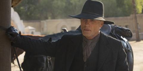 The Man In Black looking serious standing next to horse and carriage in Westworld