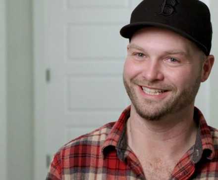 Patrick's brother John Mcmanus from 90 Day Fiancé smiling in red plaid shirt and black hat.