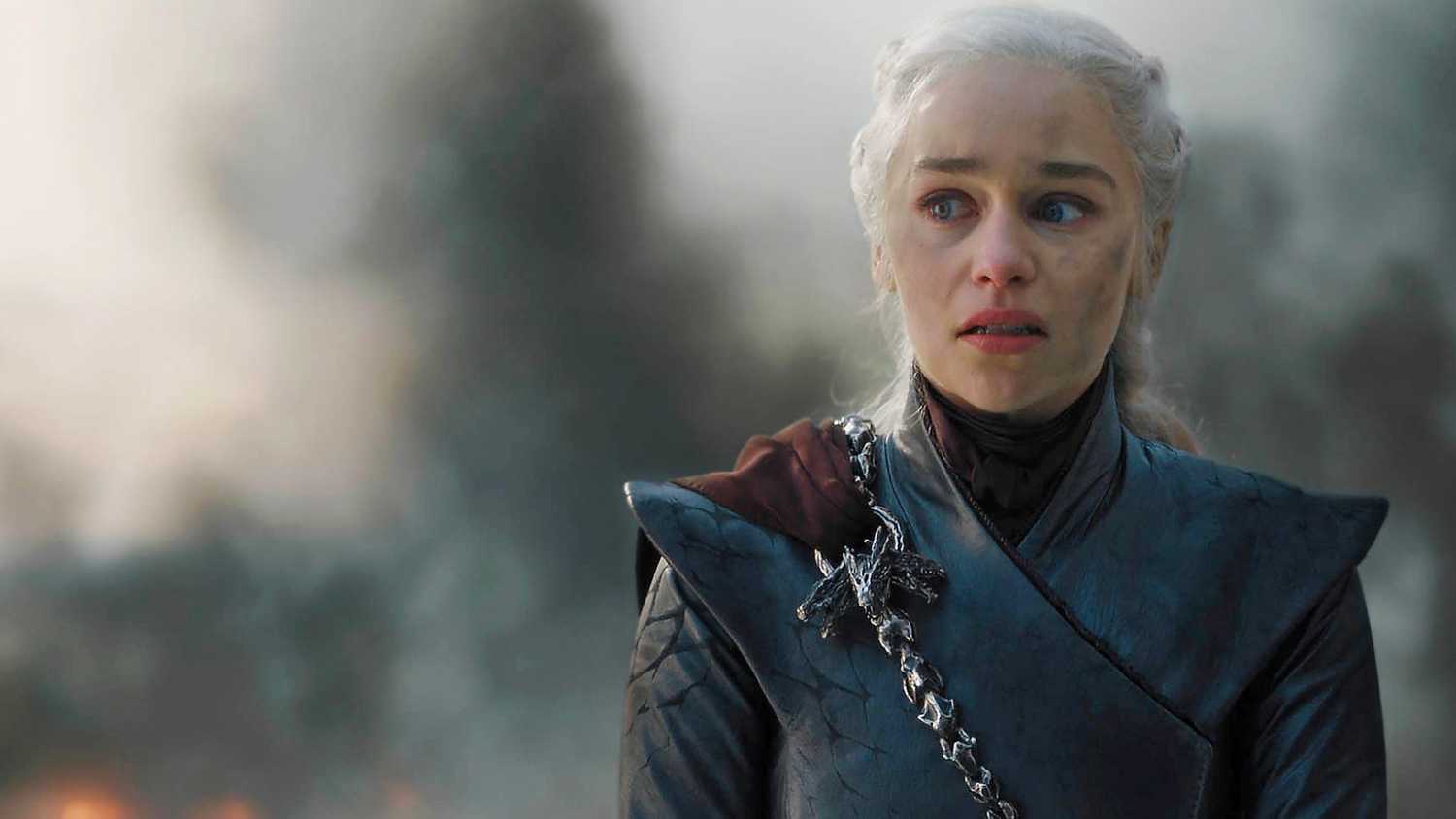 Daenerys Targaryen looking emotional while smoke blows behind her in Game of Thrones.