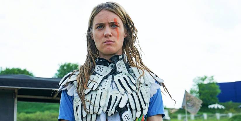 Mackenzie Davis como Kirsten em Station Eleven olha severamente com um colete feito de luvas