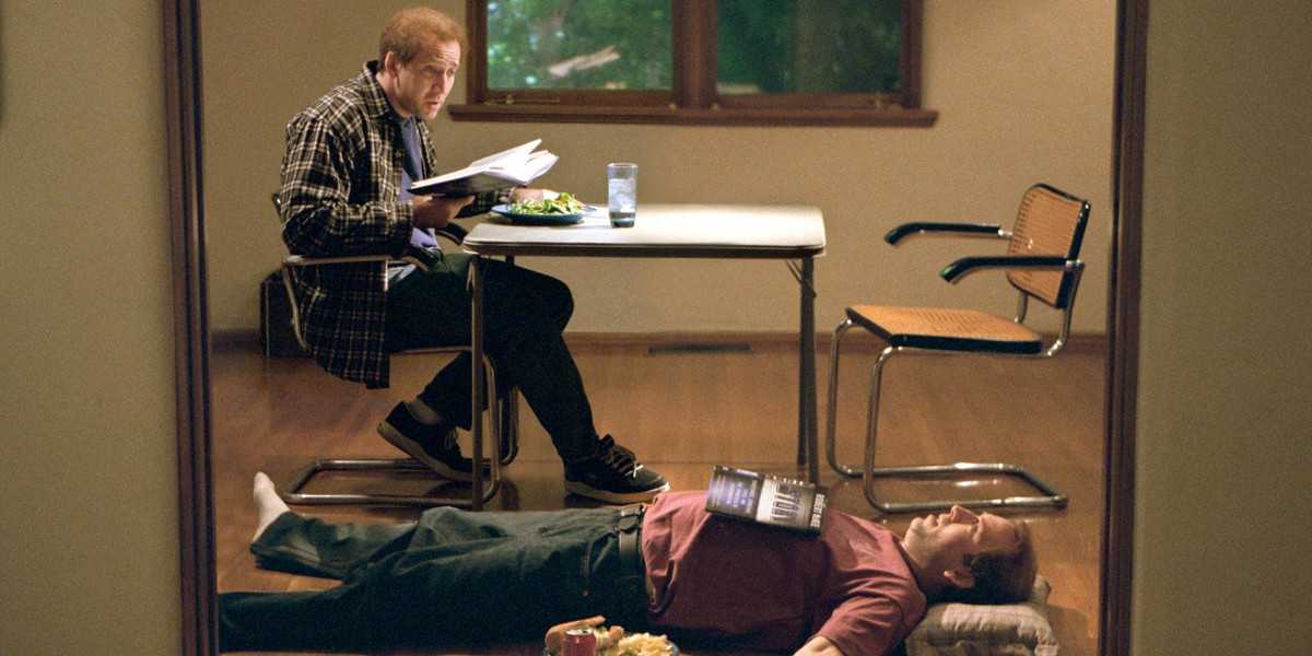 Nicolas Cage as Donald Kaufman at a table looking at Charlie Kaufman lying on the floorin Adaptation