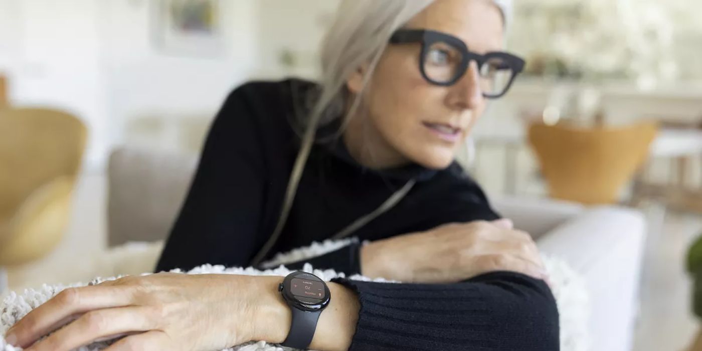 Une femme plus âgée aux cheveux blancs et un pull noir portant la Google Pixel Watch.