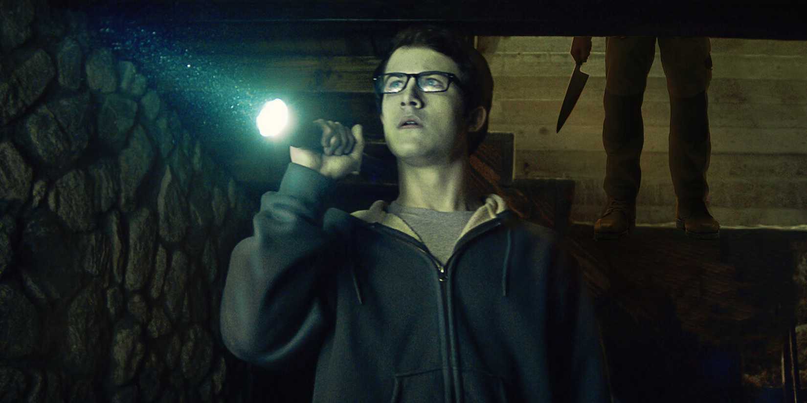 Dylan Minette's Logan stands holding a flashlight as someone approaches him with a knife in The Open House