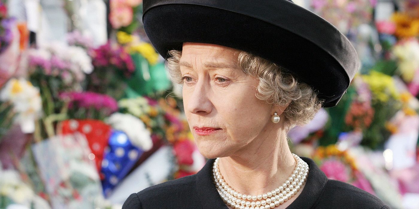 Helen Mirren as Queen Elizabeth in The Queen wearing black clothes and a pearl necklace standing in front of a wall of flowers